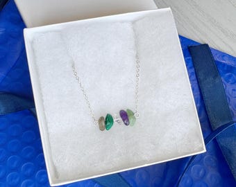 May include: A silver-toned chain necklace featuring a central arrangement of five small, polished, irregular-shaped gemstone beads in shades of brown, green, purple, and light green, resting inside a white square gift box with white padding.