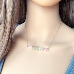 May include: A gold chain necklace with a delicate bar of pink and green gemstones.