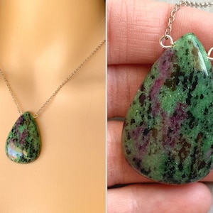 May include: A teardrop-shaped green and pink gemstone pendant necklace on a silver chain. The pendant has a speckled pattern of green, pink, and black.