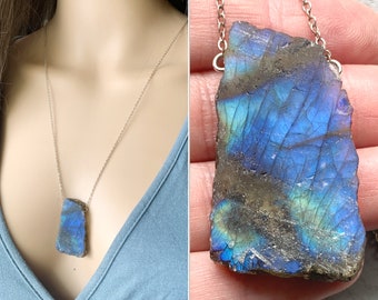 Puede incluir: Un collar de cadena de plata con un gran colgante de labradorita azul iridiscente. El colgante es una piedra natural de corte tosco con una forma irregular única.