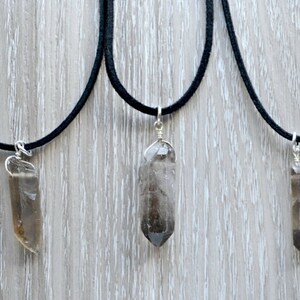 May include: Three necklaces with smoky quartz crystal pendants on black cords. The crystals are all different shapes and sizes.