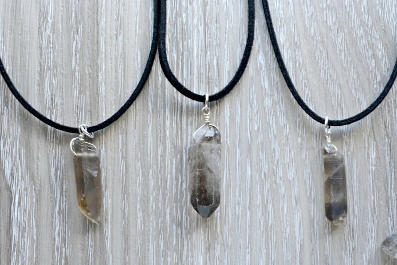 May include: Three necklaces with smoky quartz crystal pendants on black cords. The crystals are all different shapes and sizes.