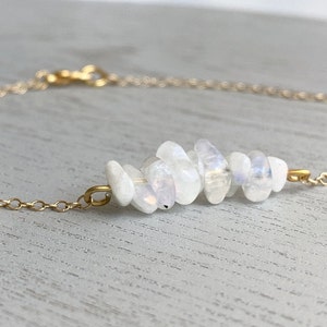 May include: A delicate gold chain necklace featuring a cluster of white moonstone beads. The beads are arranged in a staggered pattern, creating a unique and eye-catching design.