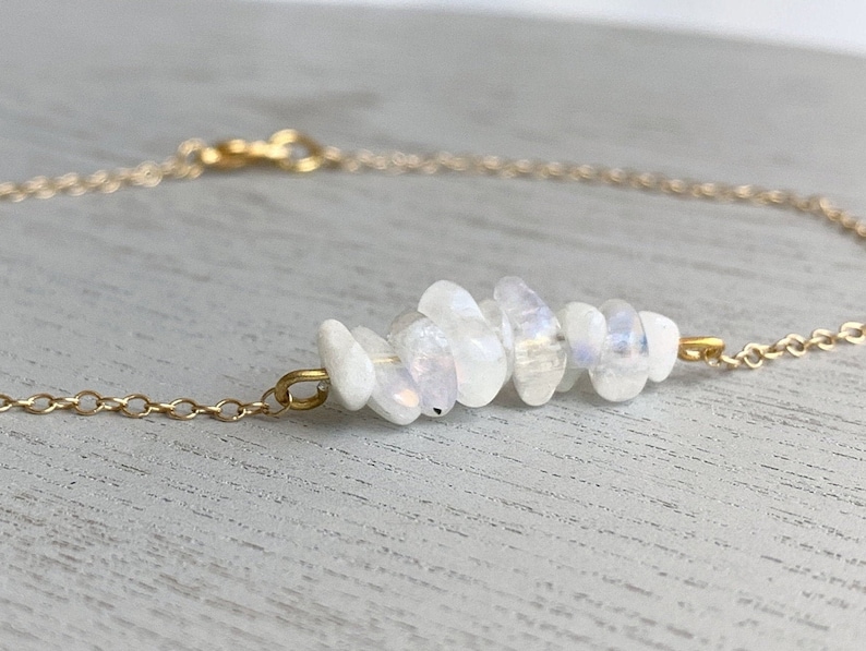 May include: A delicate gold chain necklace featuring a cluster of white moonstone beads. The beads are arranged in a staggered pattern, creating a unique and eye-catching design.
