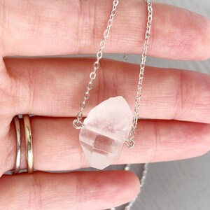 May include: A silver chain necklace with a clear quartz crystal pendant. The crystal is a natural, rough-cut shape.