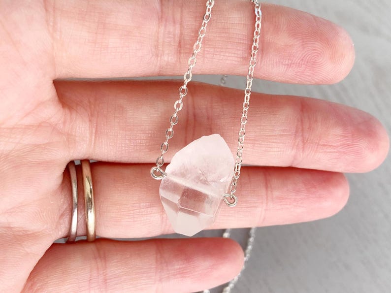 May include: A silver chain necklace with a clear quartz crystal pendant. The crystal is a natural, rough-cut shape.