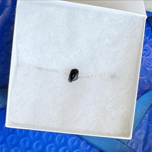 Peut inclure: Un bracelet &agrave; cha&icirc;ne argent&eacute;e d&eacute;licat comportant une seule petite perle en pierre noire polie au centre. Le bracelet est pr&eacute;sent&eacute; dans une bo&icirc;te blanche avec une doublure blanche douce et textur&eacute;e, contrastant avec la pierre sombre.