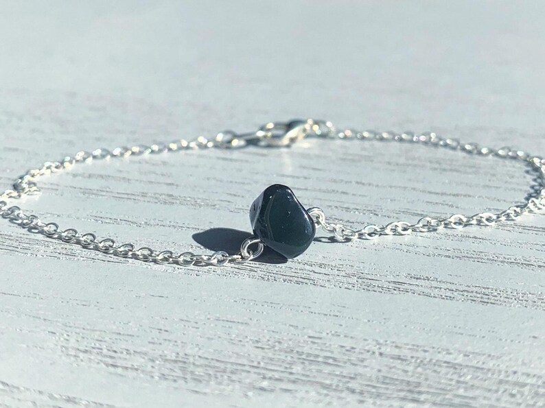 Peut inclure: Un bracelet &agrave; cha&icirc;ne fine en argent orn&eacute; d'une perle de pierre noire polie et irr&eacute;guli&egrave;re centr&eacute;e sur les maillons. Le bracelet est dot&eacute; d'un petit fermoir mousqueton en argent, pr&eacute;sentant un design simple et &eacute;pur&eacute;.