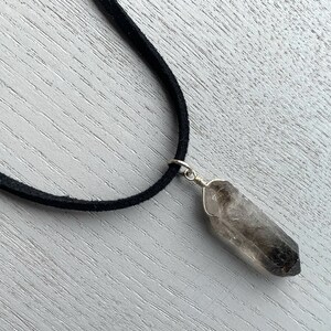 May include: A black suede cord necklace with a smoky quartz crystal pendant.