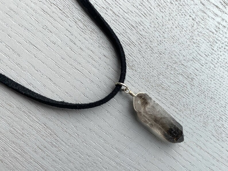 May include: A black suede cord necklace with a smoky quartz crystal pendant.