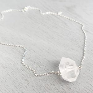 May include: A silver chain necklace with a clear quartz crystal pendant. The crystal is faceted and has a natural, irregular shape.