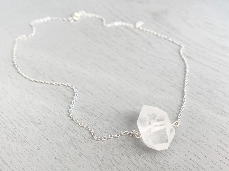 May include: A silver chain necklace with a clear quartz crystal pendant. The crystal is faceted and has a natural, irregular shape.