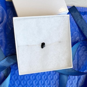 Peut inclure: Un bracelet &agrave; cha&icirc;ne fine en argent orn&eacute; d'une unique petite perle en pierre noire polie au centre. Le bracelet est pr&eacute;sent&eacute; dans une bo&icirc;te cadeau carr&eacute;e blanche avec un insert en mousse blanche, offrant une pr&eacute;sentation sobre et &eacute;pur&eacute;e.
