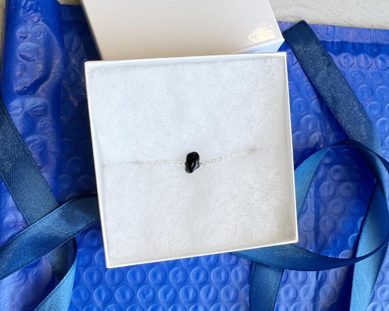 Peut inclure: Un bracelet &agrave; cha&icirc;ne fine en argent orn&eacute; d'une unique petite perle en pierre noire polie au centre. Le bracelet est pr&eacute;sent&eacute; dans une bo&icirc;te cadeau carr&eacute;e blanche avec un insert en mousse blanche, offrant une pr&eacute;sentation sobre et &eacute;pur&eacute;e.