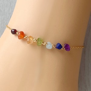 May include: A gold chain bracelet with seven different coloured gemstone beads. The beads are in a rainbow order, starting with red and ending with purple.