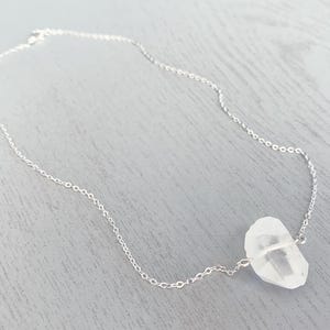 May include: A silver chain necklace with a clear quartz crystal pendant.