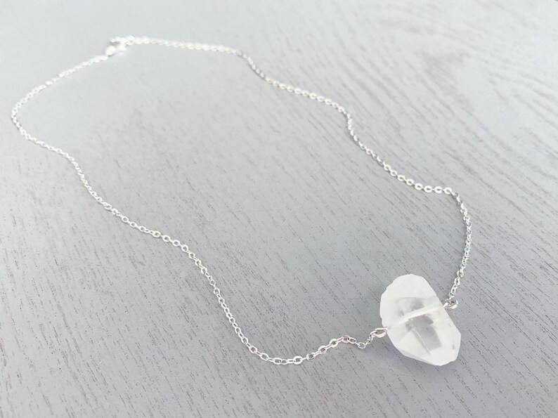 May include: A silver chain necklace with a clear quartz crystal pendant.