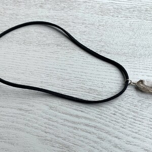 May include: A black suede cord necklace with a clear quartz crystal pendant.