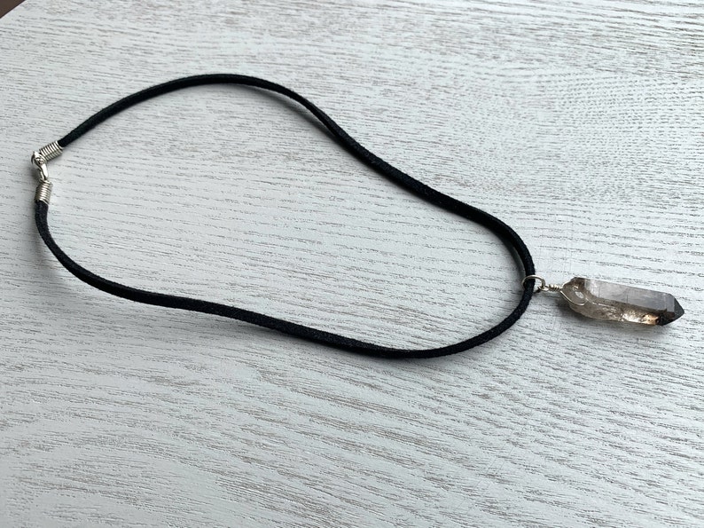 May include: A black suede cord necklace with a clear quartz crystal pendant.