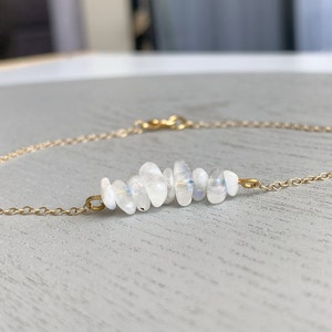 May include: A delicate gold chain bracelet featuring a row of white moonstone beads. The beads are arranged in a curved shape, creating a unique and elegant design.