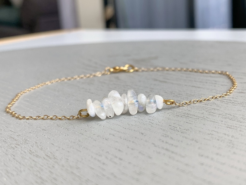 May include: A delicate gold chain bracelet featuring a row of white moonstone beads. The beads are arranged in a curved shape, creating a unique and elegant design.