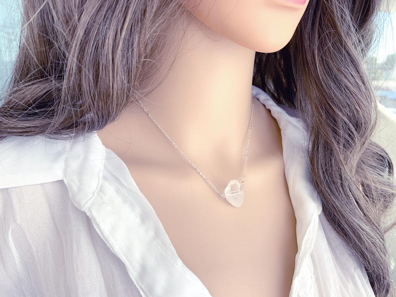 May include: A silver chain necklace with a clear quartz crystal pendant. The pendant is a natural, irregular shape.
