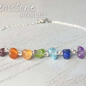 May include: A silver chain anklet with seven gemstones in rainbow colours. The gemstones are red, orange, yellow, green, blue, light blue, and purple.