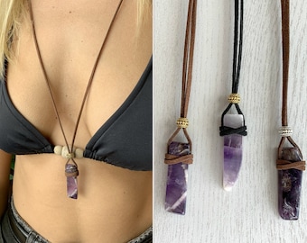 Puede incluir: Tres colgantes de cristal de amatista en cordones de cuero. Los cordones son marrones, negros y marrones. Los cristales son todos de diferentes formas y tamaños.