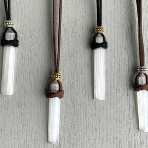 Puede incluir: Cuatro colgantes de cristal de selenita en cordones de diferentes colores. Cada colgante est&aacute; atado con un nudo y tiene una cuenta de metal en la parte superior. Los cordones son marr&oacute;n, negro, marr&oacute;n y negro.