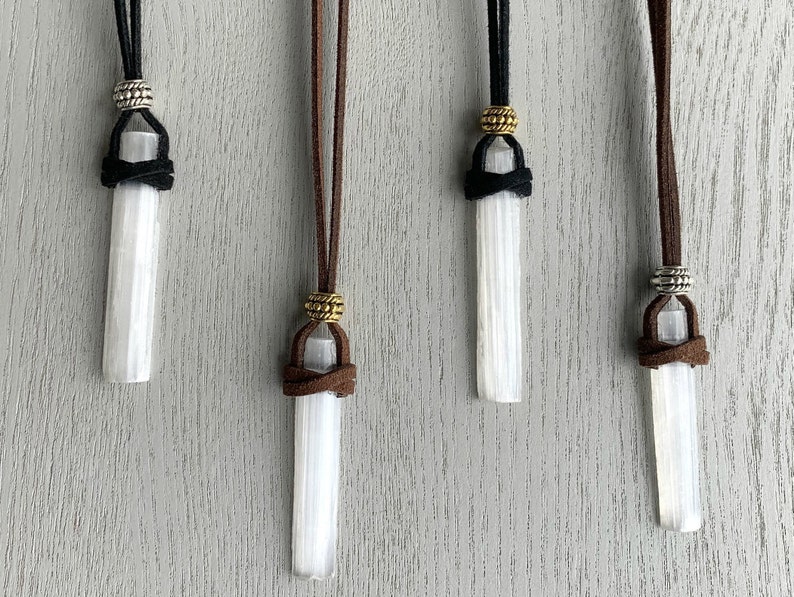 Puede incluir: Cuatro colgantes de cristal de selenita en cordones de diferentes colores. Cada colgante est&aacute; atado con un nudo y tiene una cuenta de metal en la parte superior. Los cordones son marr&oacute;n, negro, marr&oacute;n y negro.