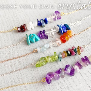 May include: Six different necklaces with various colored crystals strung on delicate chains. The crystals are arranged in a line and include amethyst, turquoise, clear quartz, aquamarine, green aventurine, and carnelian.