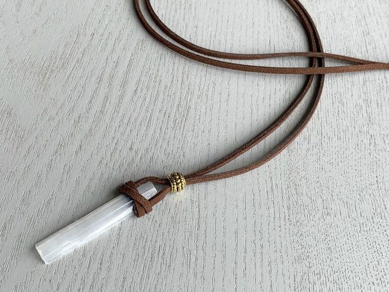 Puede incluir: Un colgante de cristal de selenita blanco en un cord&oacute;n de cuero marr&oacute;n con una cuenta dorada.