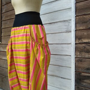 Puede incluir: Una falda a rayas con una cintura negra. La falda est&aacute; hecha de una tela ligera y tiene un corte holgado y fluido. La falda es rosa y verde con rayas horizontales.