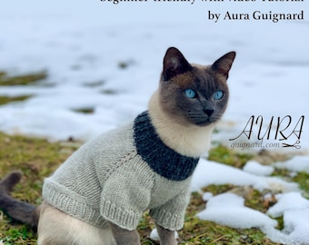May include: A Siamese cat wearing a gray and navy blue knitted sweater, sitting on green grass with snow in the background. The image includes text that reads "Cat or Small Dog Sweater/Jumper PDF knitting pattern beginner-friendly with video Tutorial by Aura Guignard."