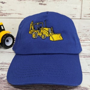 May include: A blue baseball cap with a yellow embroidered image of a backhoe excavator.