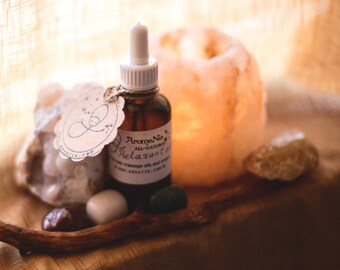 Puede incluir: Una botella de vidrio marrón con un gotero y una etiqueta blanca que dice "Aroma No. 5 Aceite Relajante Natural". La botella está sobre una superficie de madera con una roca grande, una roca pequeña y una piedra verde.