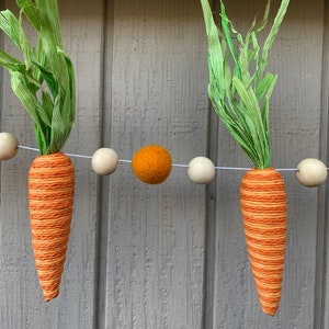 May include: A garland of orange and white felt balls with carrot-shaped decorations and green paper leaves.