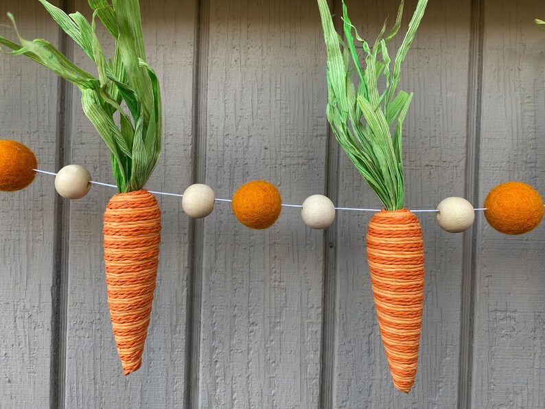 May include: A garland of orange and white felt balls with carrot-shaped decorations and green paper leaves.
