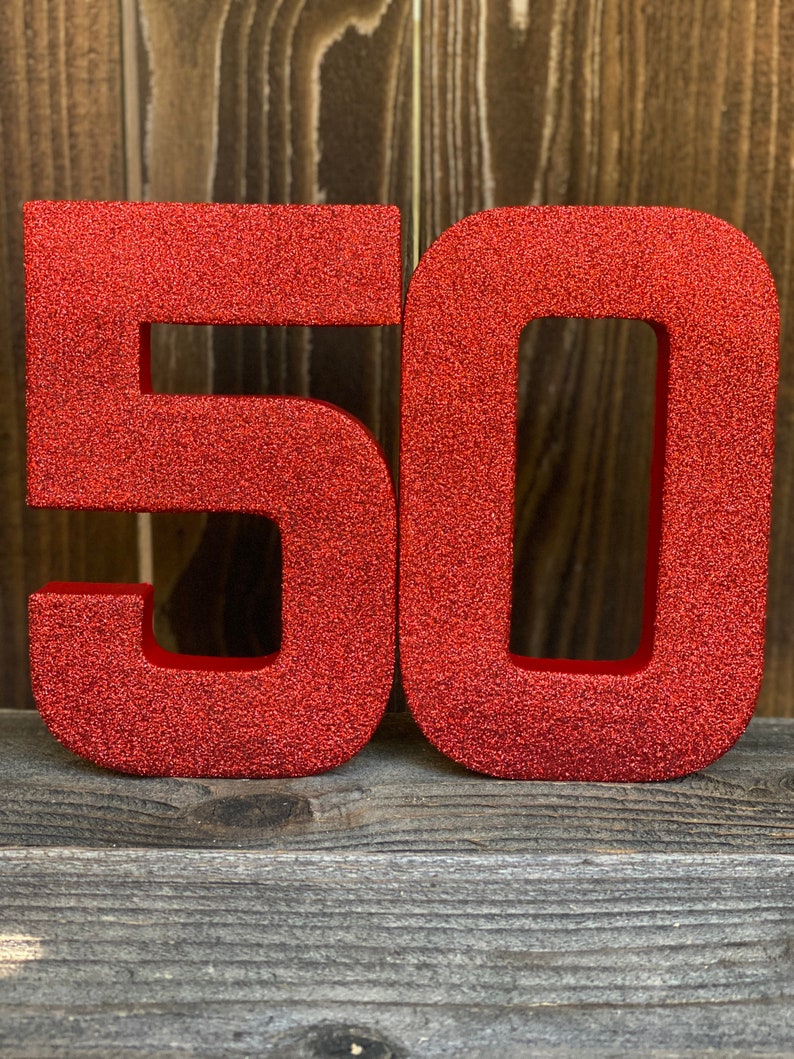 May include: Red glitter number 50, the numbers are standing upright on a wooden surface.