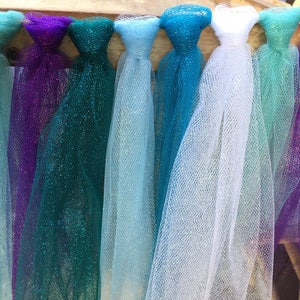 Puede incluir: Un conjunto de serpentinas de tul en varios tonos de azul, verde, morado y blanco. Las serpentinas est&aacute;n atadas juntas y tienen un acabado brillante.