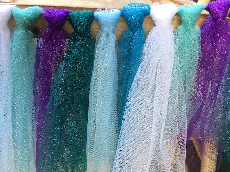 Puede incluir: Un conjunto de serpentinas de tul en varios tonos de azul, verde, morado y blanco. Las serpentinas est&aacute;n atadas juntas y tienen un acabado brillante.