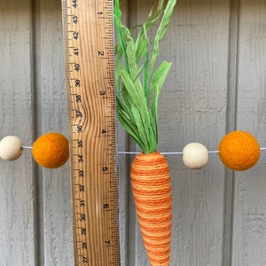 May include: A felt carrot garland with orange and white felt balls and a green felt stem. The carrot is approximately 7 inches long.