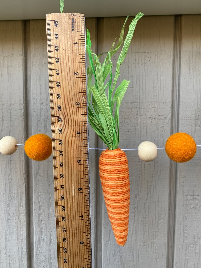 May include: A felt carrot garland with orange and white felt balls and a green felt stem. The carrot is approximately 7 inches long.