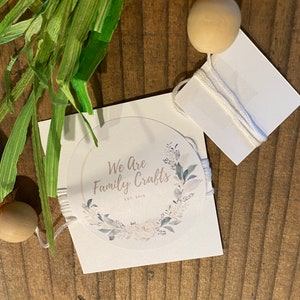 May include: A white card with a round sticker featuring a floral wreath and the text "We Are Family Crafts Est. 2015".