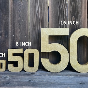 May include: Four gold glitter cardboard numbers, 50, in four different sizes: 4 inches, 8 inches, 16 inches. The numbers are arranged from smallest to largest.