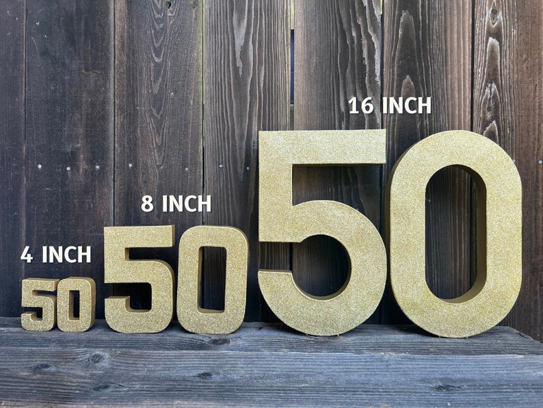 May include: Four gold glitter cardboard numbers, 50, in four different sizes: 4 inches, 8 inches, 16 inches. The numbers are arranged from smallest to largest.