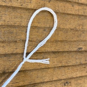May include: A white string tied in a loop with the ends of the string fanned out.