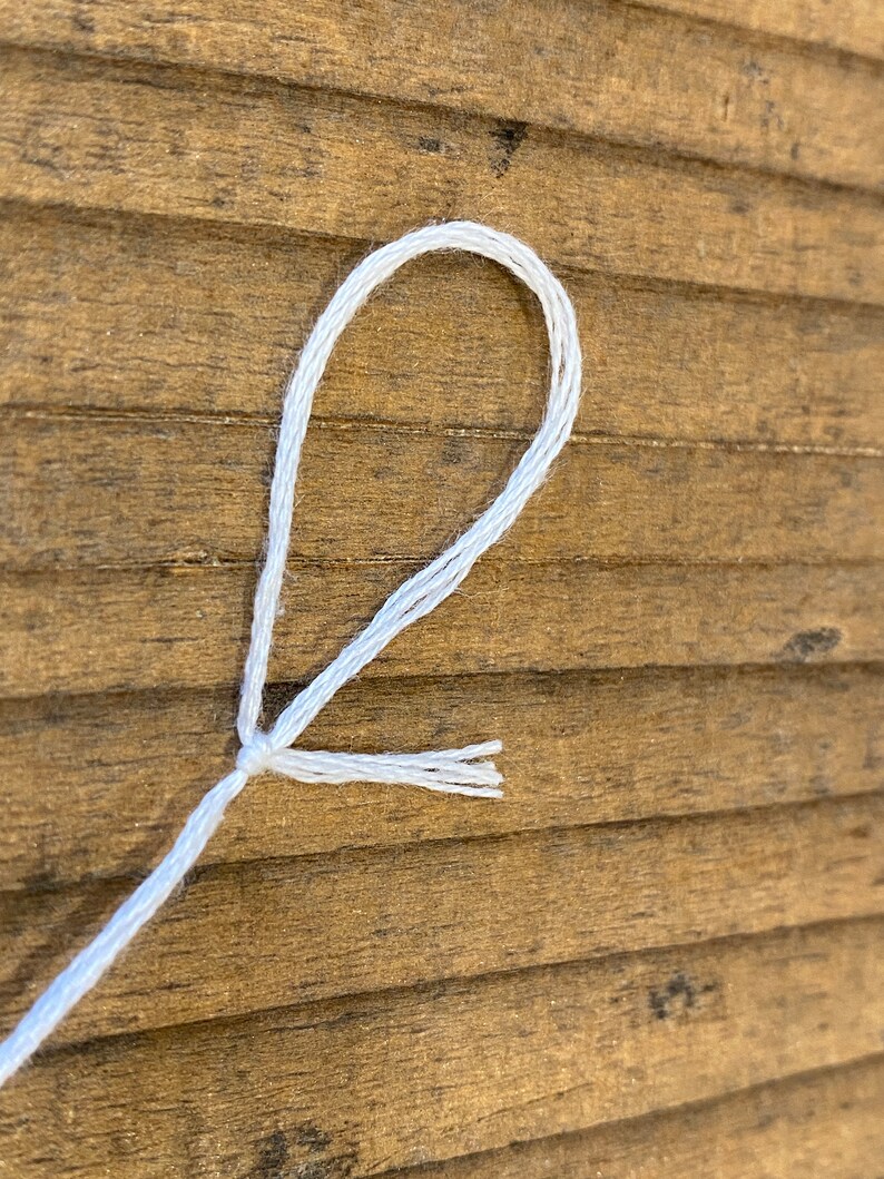 May include: A white string tied in a loop with the ends of the string fanned out.