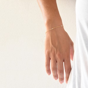 Könnte beinhalten: Ein zartes Armband aus goldener Kette mit kleinen weißen Perlen.