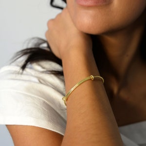 Könnte beinhalten: Ein goldenes Armreif-Armband mit einem einfachen Knotendesign.